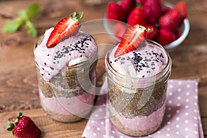 Lilac smoothie with strawberry, baÃâanas and chia pudding in two jars on wooden background