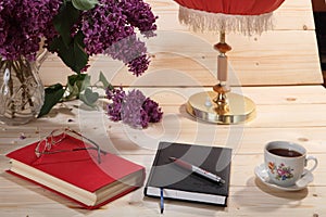 Lilacs, book, notebook, spectacles, cup of tea and table lamp