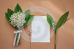 Lily of the valley and empty notepad with text copy space on beige background