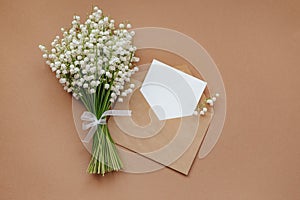 Lily of the valley and empty paper with text copy space on beige background