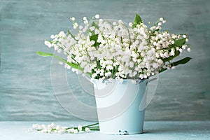 Lily of the valley flowers in blue vase on rustic table. Spring aroma bouquet