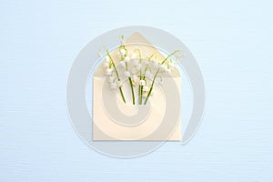 Lily of the valley flowers in envelope on blue background, view from above. Romantic love letter concept