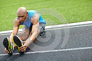 Limbering up before the run. Full length shot of a male athlete stretching his muscles at the race track.