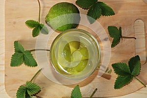 Lime in glass goblets and fruit with mint on a wooden table.