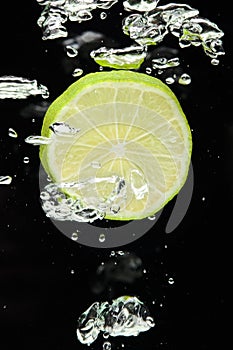 Lime (lemon) falling in water on black