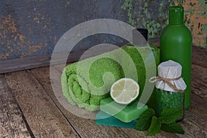 Lime mint composition of beauty threatment products in green colors on brown wooden background: shampoo, soap, bath salt, towel, o