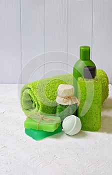 Lime mint composition of beauty threatment products in green colors on a white concrete background: shampoo, soap, bath salt, towe