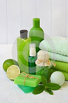 Lime mint composition of beauty threatment products in green colors on a white concrete background: shampoo, soap, bath salt, towe photo