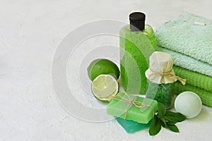 Lime mint composition of beauty threatment products in green colors on a white concrete background: shampoo, soap, bath salt, towe