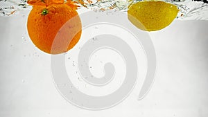 Lime and orange are dropping in water on isolated background. Video citrus in slow motion.