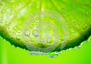 Lime slice with drop of lemon juice close-up. Fresh and juicy Citrus over green background. Dripping lime juice closeup