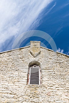 Limestone facade of ancient church with window shutter and cross