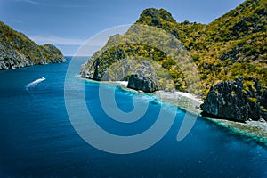 Limestone karst coastline of Matinloc Island with tourist boats in ocean strait. El Nido, Palawan, Philippines. Drone