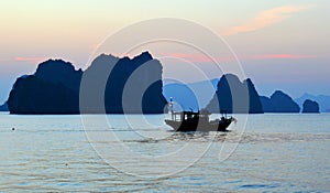 Limestone karsts and fishing boat in silhouette at sunset, Halong Bay Vietnam