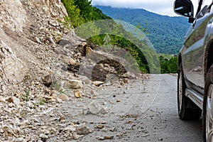 Limestone rockfall and landslide fallen on a tarmac road with car driving past