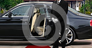 Limo driver standing next to opened car door with red carpet