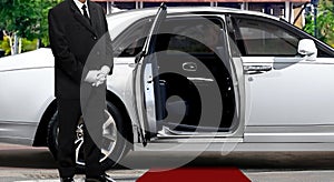 Limo driver standing next to opened car door with red carpet photo