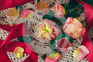 Limp roses with red ribbon and marmalade on a white lace doily in vintage style