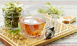 Linden cup of herbal healing tea with lime tree bloom and glass can with dried herb