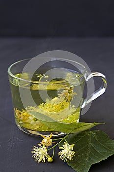Linden flowers tea.Cup of hot herbal tea with linden fresh flowers on a black table