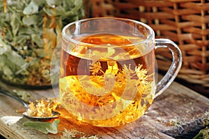 Linden herbal tea with flowers in a glass cup on wooden rustic board with lime blossom dry herb