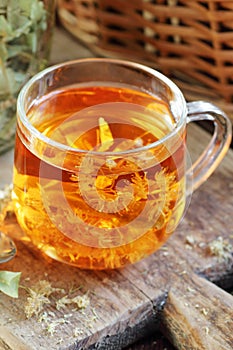 Linden herbal tea with flowers in a glass cup on wooden rustic board with lime blossom dry herb