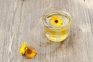 Linden honey in jar and calendula blossoms on wooden table