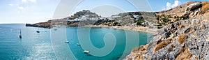 Lindos bay with famous beach and village of Lindos and Acropolis in background â€“ panoramic Rhodes, Greece