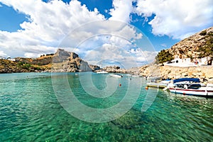 Lindos â€“ view of St. Paul bay, motor boats anchored near orthodox church and acropolis of Lindos in background Rhodes, Greece