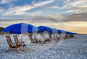 A line of beach umbrellas and chairs on an empty beach at sunrise