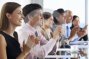 Line Of Business People Listening To Presentation Seated At Glass Boardroom Table