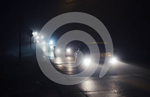 Line of cars in fog, with shining headlights in a foggy night