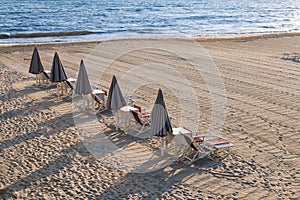 Line of closed beach umbrellas lougners, chairs and sunbeds