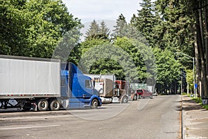 Line of different big rigs semi trucks and semi trailers standing on the forest rest area parking lot for take a brake