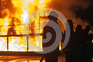Line of firefighters standing with hose in front of a burning structure during firefighting exercise