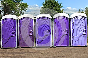 Line of Five Purple and Lavender Colored Portable Toilets