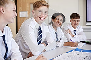 Line Of High School Students Wearing Uniform Sitting At Desk In Classroom