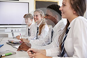 Line Of High School Students Wearing Uniform Sitting At Desk In Classroom