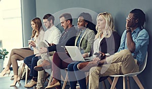 In the line for the interview. a group of businesspeople using different wireless devices while waiting in line for an