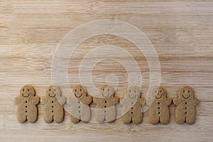 Line of plain gingerbread cookies with faces on wooden table with copy space