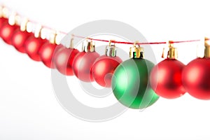 Line of red christmas balls and one green ball on white background. Christmas decorations.