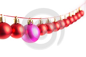 Line of red christmas balls and one lilac or purple ball on white background. Christmas decorations.