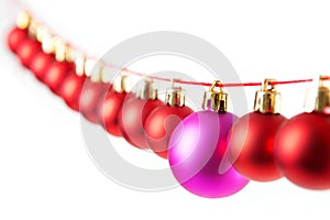 Line of red christmas balls and one lilac or purple ball on white background. Christmas decorations.