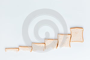 A line of slices of bread which are getting bigger and bigger, on a white background