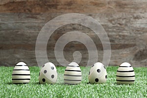 Line of traditional Easter eggs decorated with black paint on green lawn against wooden background