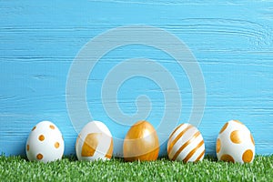 Line of traditional Easter eggs decorated with golden paint on green lawn near wooden wall