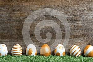 Line of traditional Easter eggs decorated with golden paint on green lawn near wooden wall