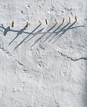 A line of wooden pegs on a rope washing line with a textured white wall behind