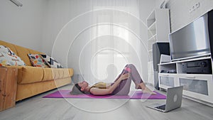 On-line work out woman using internet services with help of her instructor. Slim woman lays down with resistance band