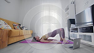 On-line work out woman using internet services with help of her instructor. Slim woman stands in bridge pose and spread